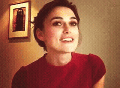 A Woman Wearing A Red Shirt Is Smiling In Front Of A Picture On The Wall GIF