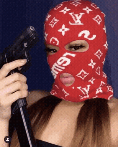 A Woman Wearing A Red Ski Mask Is Holding A Gun GIF