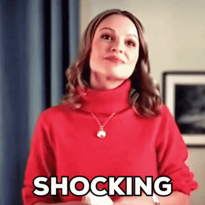 A Woman Wearing A Red Sweater And Necklace Is Making A Shocking Face . GIF