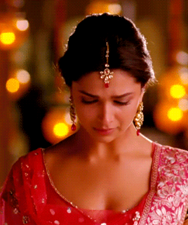 A Woman Wearing A Red Top And Gold Earrings Looks Down At Something GIF