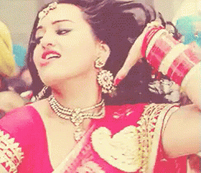 A Woman Wearing A Red Top And Gold Jewelry Is Smiling GIF