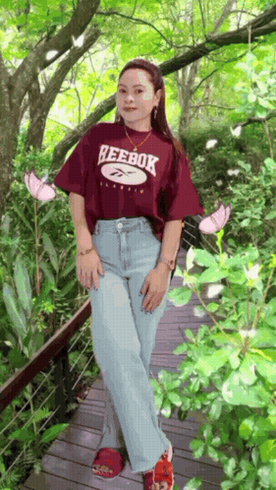 A Woman Wearing A Reebok T-Shirt Is Standing On A Wooden Bridge GIF