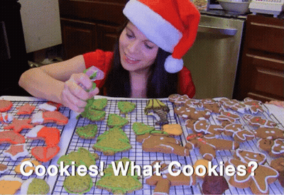 A Woman Wearing A Santa Hat Decorates Gingerbread Cookies With The Words Cookies What Cookies Below Her GIF