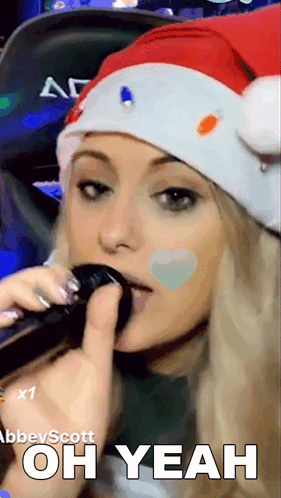 A Woman Wearing A Santa Hat Is Singing Into A Microphone With The Words Oh Yeah Below Her GIF