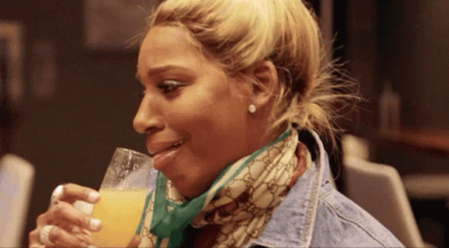 A Woman Wearing A Scarf And A Denim Jacket Is Drinking Orange Juice GIF