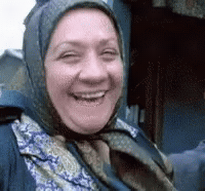 A Woman Wearing A Scarf And A Head Scarf Is Smiling For The Camera . GIF