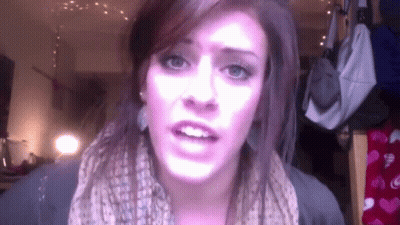 A Woman Wearing A Scarf And Earrings Looks At The Camera GIF