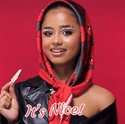A Woman Wearing A Scarf Around Her Head Is Holding A Piece Of Food And Says It 'S Nice GIF