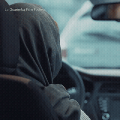 A Woman Wearing A Scarf Is Driving A Car With La Guarimba Film Festival Written On The Bottom Of The Image GIF