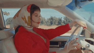 A Woman Wearing A Scarf Is Driving A Car . GIF