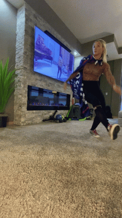A Woman Wearing A Scarf That Says ' Oakland ' On It Is Jumping In Front Of A Television GIF