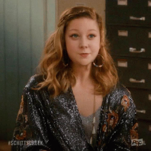 A Woman Wearing A Sequined Jacket And Hoop Earrings Is Sitting In Front Of A Filing Cabinet . GIF