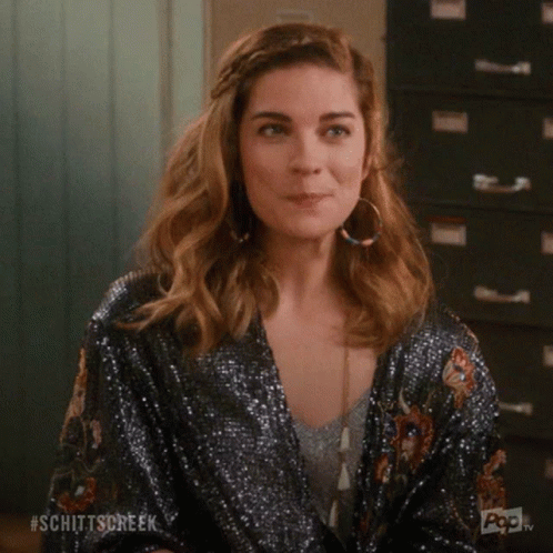 A Woman Wearing A Sequined Kimono And Hoop Earrings Is Smiling And Making A Funny Face . GIF