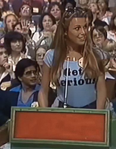 A Woman Wearing A Shirt That Says " Let 'S Be Serious " Stands In Front Of A Microphone GIF