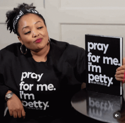 A Woman Wearing A Shirt That Says Pray For Me I 'M Petty Is Holding A Book GIF