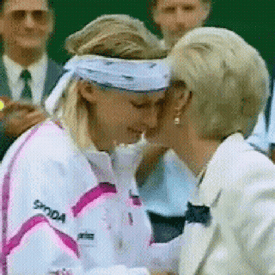 A Woman Wearing A Skoda Jacket Is Kissing Another Woman On The Cheek GIF