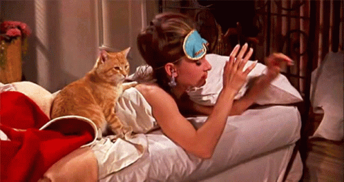 A Woman Wearing A Sleep Mask Is Laying On A Bed Next To A Cat GIF