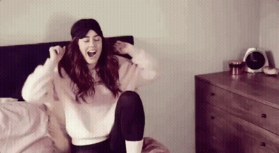 A Woman Wearing A Sleep Mask Is Sitting On A Bed With Her Legs Crossed . GIF