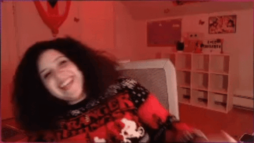 A Woman Wearing A Stranger Things Sweater Is Sitting On A Couch . GIF