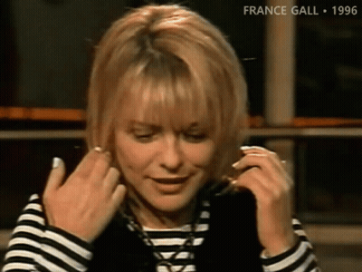 A Woman Wearing A Striped Shirt And A Black Vest Adjusts Her Hair GIF