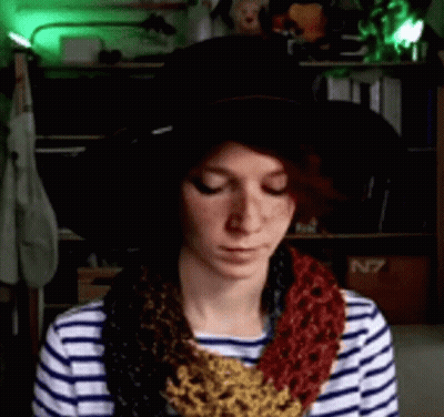 A Woman Wearing A Striped Shirt And A Hat With A Scarf Around Her Neck Is Looking Down GIF