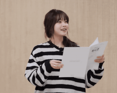 A Woman Wearing A Striped Sweater Holds A Piece Of Paper And Says Gracias In A Foreign Language GIF