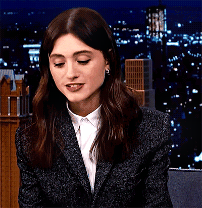 A Woman Wearing A Suit And A White Shirt Is Smiling At The Camera . GIF