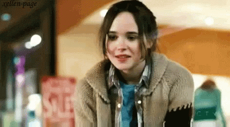 A Woman Wearing A Sweater And A Blue Shirt Is Standing In Front Of A Sign That Says Sale . GIF