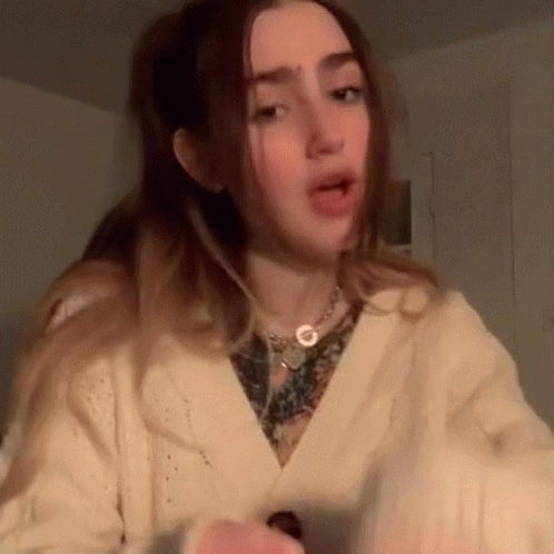 A Woman Wearing A Sweater And A Necklace Is Making A Face . GIF