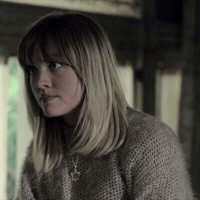 A Woman Wearing A Sweater And A Necklace With A Pendant That Looks Like A Frog GIF