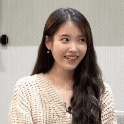 A Woman Wearing A Sweater And Earrings Is Smiling And Looking At The Camera . GIF