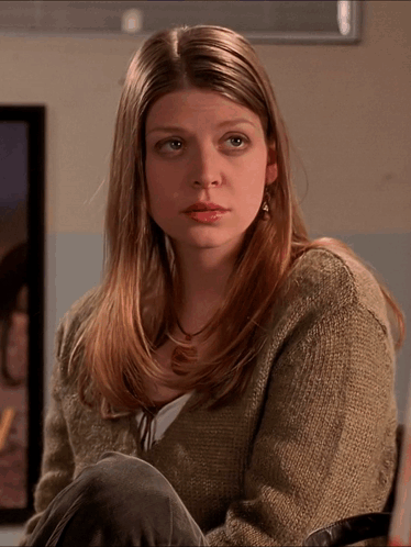 Woman In Sweater And Earrings Sitting In Front Of Framed Picture GIF
