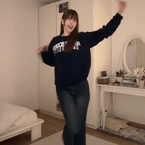 A Woman Wearing A Sweater That Says " Abercrombie & Fitch " Is Dancing In A Bedroom GIF