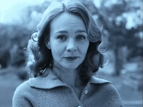 A Woman Wearing A Sweater With Buttons On The Front Looks At The Camera GIF
