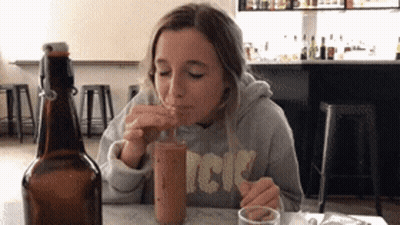 A Woman Wearing A Sweatshirt That Says Acdc Drinks From A Bottle GIF