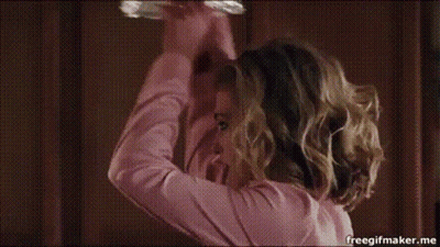 A Woman Wearing A Tiara And A Pink Shirt Is Making A Funny Face In A Kitchen . GIF