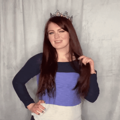 A Woman Wearing A Tiara And A Striped Shirt Holds Her Hair GIF