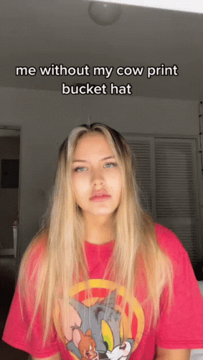 A Woman Wearing A Tom And Jerry Shirt Says " Me Without My Cow Print Bucket Hat " On The Bottom GIF