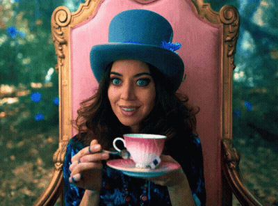 A Woman Wearing A Top Hat Is Sitting In A Chair Drinking From A Teacup GIF