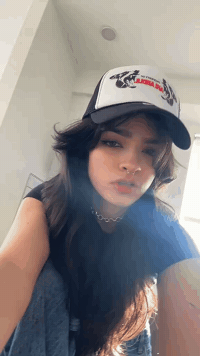 A Woman Wearing A Trucker Hat And A Nose Ring Is Kneeling Down . GIF
