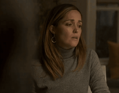 A Woman Wearing A Turtleneck Sweater And Earrings Is Sitting At A Table With Her Mouth Open . GIF