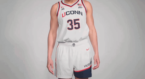 A Woman Wearing A Uconn Basketball Jersey Holds Her Hands To Her Chest GIF