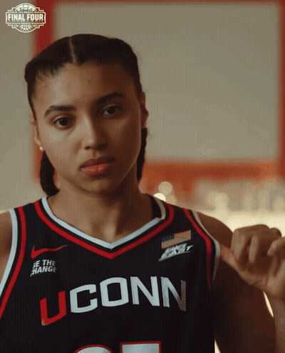 A Woman Wearing A Uconn Basketball Jersey Looks At The Camera GIF