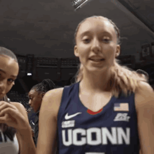A Woman Wearing A Uconn Basketball Jersey Looks At The Camera GIF