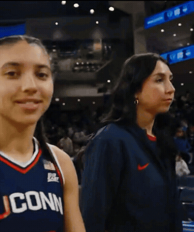 A Woman Wearing A Uconn Jersey Stands Next To A Woman Wearing A Nike Jacket GIF