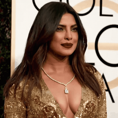 A Woman Wearing A Very Low Cut Gold Dress And A Necklace GIF