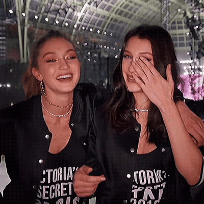 A Woman Wearing A Victoria 'S Secret Shirt Laughs With Another Woman GIF