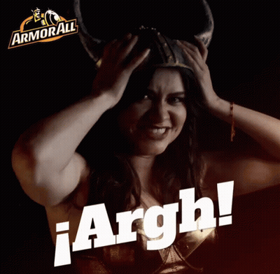A Woman Wearing A Viking Helmet Is Holding Her Head In Front Of A Sign That Says Armorall GIF