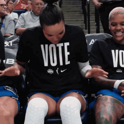 A Woman Wearing A Vote Shirt Sits In A Crowd GIF