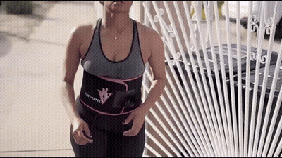 A Woman Wearing A Waist Trainer Is Standing In Front Of A Fence . GIF